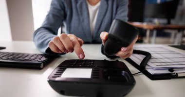 Businesswoman's Hand Dialing Telephone Number To Make Phone Call In Office