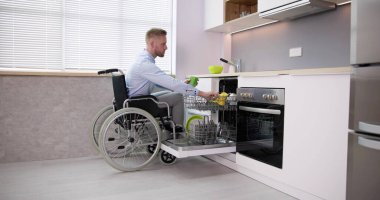 Person With Disability In Wheelchair Using Dishwasher In Kitchen
