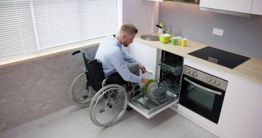 Person With Disability In Wheelchair Using Dishwasher In Kitchen