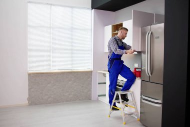 Male Carpenter Assembling White Cabinet On Wall In Kitchen