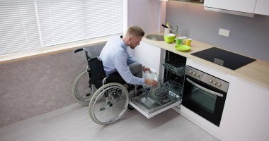 Person With Disability In Wheelchair Using Dishwasher In Kitchen