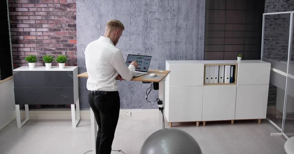 良い姿勢のためにオフィスで調節可能な高さ立ちデスクを使用して男 — ストック写真