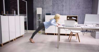 Ofis masasında şınav çeken genç bir iş kadınının yan görüntüsü