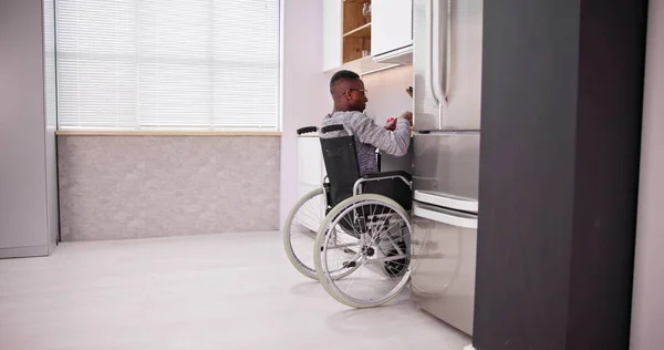若い障害者が車椅子に座ってキッチンで食べ物を準備 — ストック写真