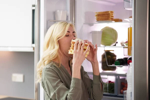 Jovem Mulher Comendo Sanduíche Frente Geladeira — Fotografia de Stock