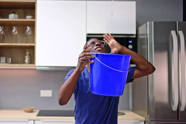 台所で天井から水滴が漏れながら心配男保持バケツ — ストック写真