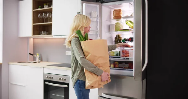 健康食品とオープン冷蔵庫の近くに立つ食料品袋を持つ女性 — ストック写真