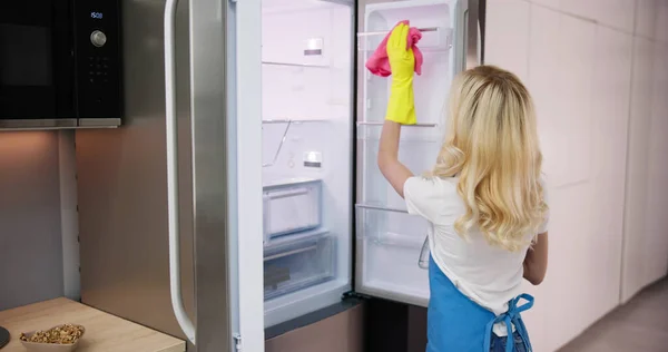 若いキッチンの冷蔵庫のクリーニング専門のクリーニング サービス女性の笑みを浮かべて — ストック写真