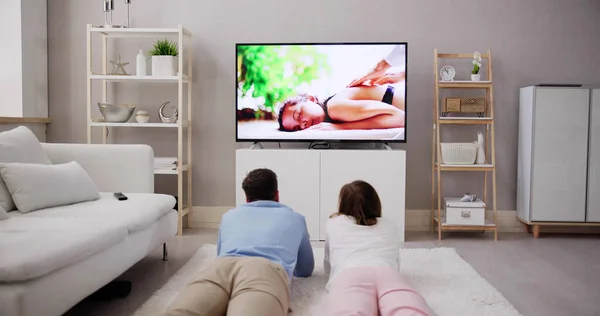 自宅のテレビで映画を見てのカーペットの上に横たわる若い幸せなカップル — ストック写真
