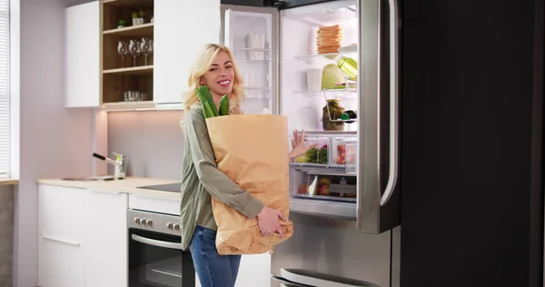 提着购物袋站在装有健康食品的开放式冰箱附近的妇女 — 图库照片