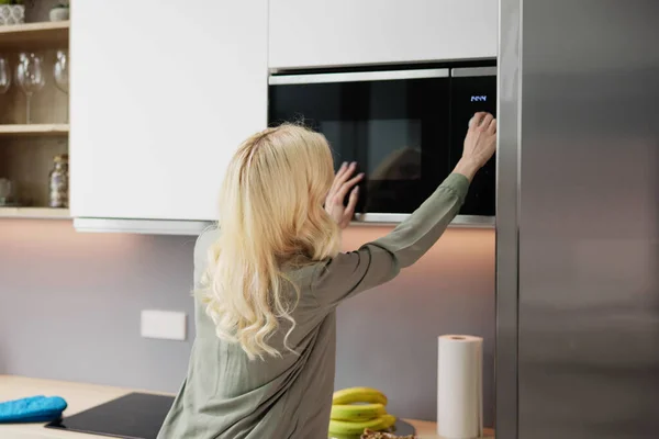 Woman Using Microwave Oven For Heating Food At Home