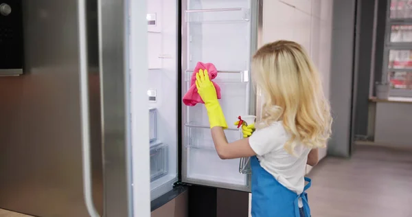 若いキッチンの冷蔵庫のクリーニング専門のクリーニング サービス女性の笑みを浮かべて — ストック写真