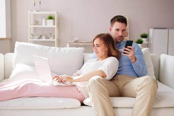家庭伴侣使用笔记本电脑和电话在沙发上 — 图库照片