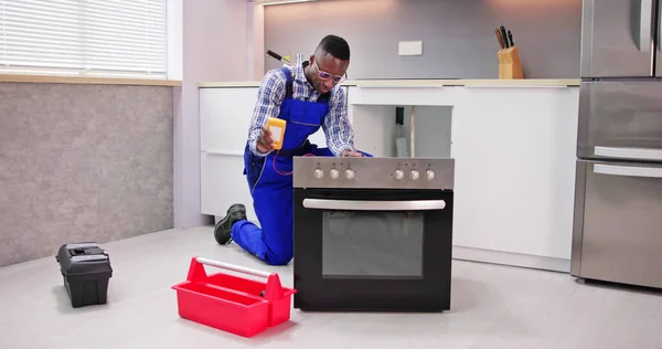 年轻男修理工在厨房里修理烤箱 — 图库照片