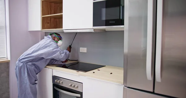 男子在病虫害防治中的表现工人在家庭厨房架子上喷洒杀虫剂 — 图库照片