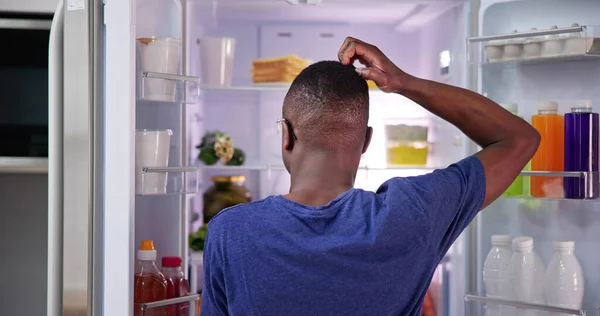 stock image Rear View Of A Confused Young Man Looking At Food In Refrigerator