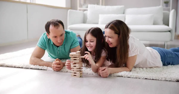 躺在地毯上玩玩家里的木制积木的幸福家庭 — 图库照片