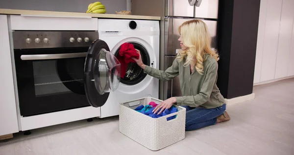 ユーティリティルームで洗濯機に汚れた服をロードする女性 — ストック写真