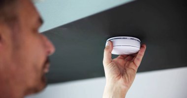 Person's Hand Installing Smoke Detector On Ceiling Wall At Home clipart