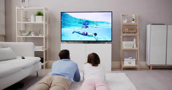 Młoda Para Szczęśliwy Leżąc Dywanie Oglądając Film Telewizji Domu — Zdjęcie stockowe