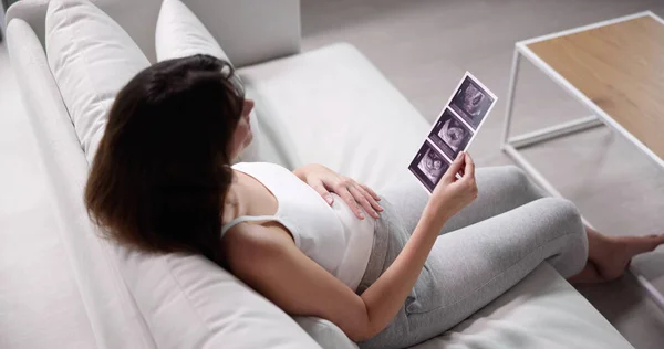 초음파를 보면서 소파에 앉아있는 임신한 여자의 클로즈업 — 스톡 사진