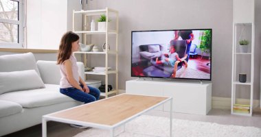 Uzaktan kumanda televizyonda film izlerken kanepede oturan çocuk