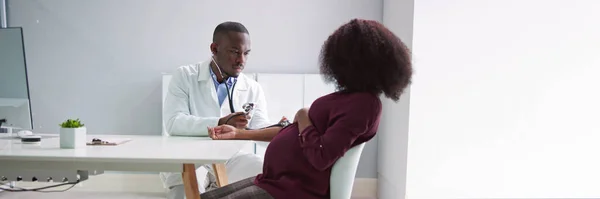 Male Doctor Measuring Blood Pressure Pregnant Woman Clinic —  Fotos de Stock