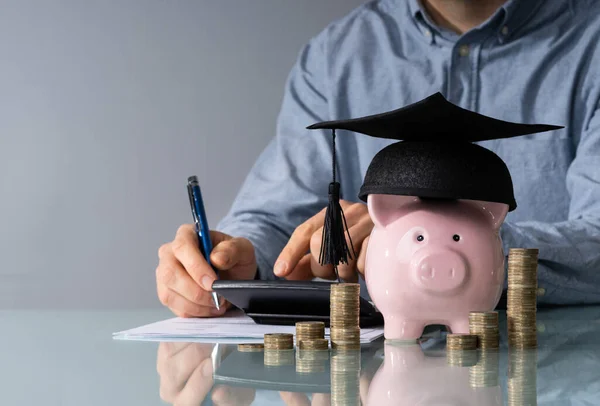 卒業の帽子と実業家の前に積み重ねられたコインを身に着けている貯金箱のクローズ アップ — ストック写真