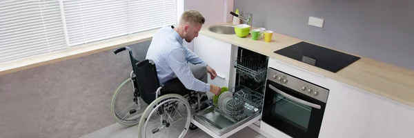 厨房使用洗碗机的轮椅上的残疾人 — 图库照片