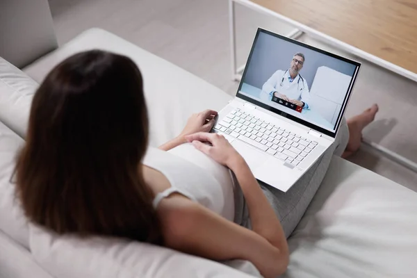 怀孕妇女与医生躺在笔记本电脑上躺在沙发视频会议上 — 图库照片