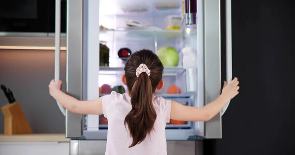 キッチンの女の子オープン冷蔵庫のドア内部を見る — ストック写真