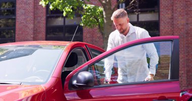 Koltuk değnekli genç adam kırmızı bir arabanın kapısını açıyor.