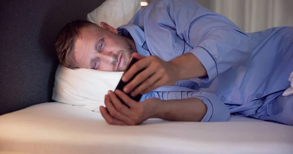 Άνθρωπος Ξαπλωμένος Στο Κρεβάτι Χρησιμοποιώντας Κινητό Τηλέφωνο Νύχτα — Φωτογραφία Αρχείου