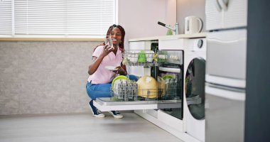 Mutlu genç kadın denetimi saydam içme cam bulaşık makinesi yakınındaki yıkanmış