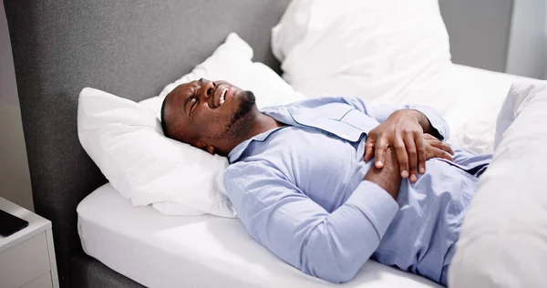 アフリカ人男性は胃の痛みに苦しんでベッドに座って — ストック写真