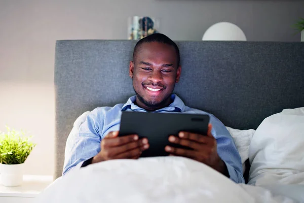デジタル タブレットのライトアップを見てベッドに横になっている男 — ストック写真