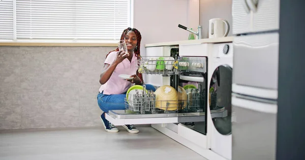 快乐的年轻女子检查洗过的透明饮料玻璃附近的洗碗机 — 图库照片