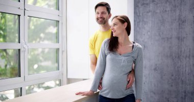 Pencerenin yanındaki Mutlu Genç Hamile Çiftin Portresi