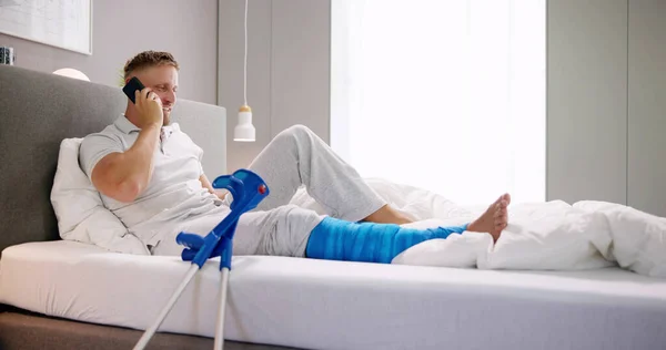 Happy Young Man Broken Leg Sitting Sofa Talking Mobile Phone — Stock Photo, Image