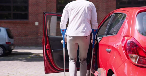 赤い車のドアを開ける松葉杖を持つ若い男 — ストック写真