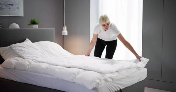 若い女性の家政婦がホテルの部屋でベッドを変える — ストック写真