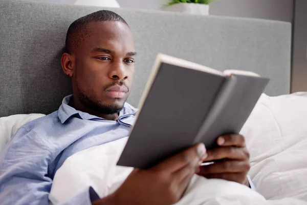 ベッドの上の彼の本を読んで幸せな若いアフリカ男 — ストック写真