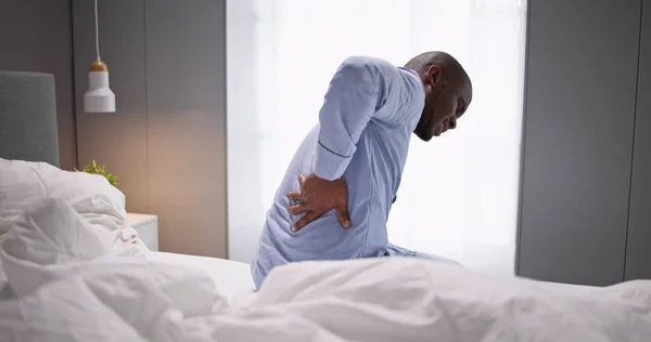 男人坐在床上从背痛中痛苦 — 图库照片