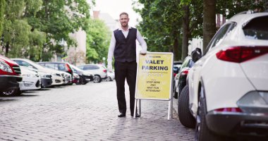 Gülümseyen bir genç erkek uşak Valet Parking işareti duran portresi