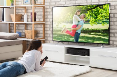 Uzaktan kumanda televizyon evde izlerken zevk Holding beyaz halı üzerinde yatan genç kadın