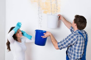 Young Woman Standing With Worker Collecting Water In Bucket From Ceiling In House clipart