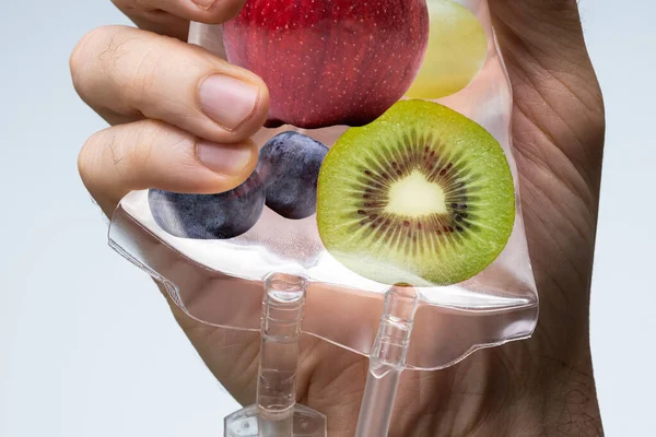 Person\'s Hand Holding Saline Bag Filled With Various Fruit Slices Against Grey Backdrop