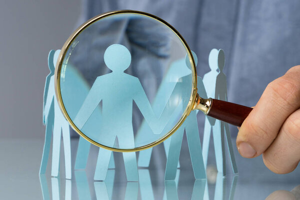 Держит увеличительное стекло и бумажных людей. Крупный план
