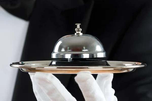 Midsection of waiter holding service bell in plate against gray background