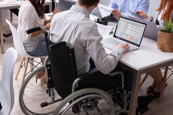 Side View Of A Disabled Businessman Sitting On Wheelchair Using Laptop Working In Office